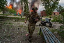 2024年5月11日、ロシア軍の激しい攻撃を受ける北東部ハルキウ州ボウチャンスクで、炎上する家の前を通るウクライナの警察官=AP