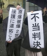 被爆2世訴訟の控訴が棄却され、福岡高裁前で「原爆被爆2世の援護に道拓こう」などと書かれた紙を掲げる原告ら＝29日午後
