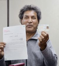 「在留特別許可」が与えられ、公布された在留カード（右）を手にするパキスタン人男性＝23日午前、東京・霞が関の司法記者クラブ