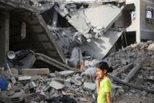 パレスチナ自治区ガザ南部ラファで、イスラエルの攻撃で壊れた建物のそばを歩く少女＝25日（ロイター＝共同）