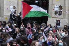 パリ政治学院の前でパレスチナの旗を振る学生ら＝26日、パリ（AP＝共同）