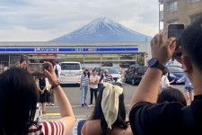 コンビニの屋根越しの富士山を撮影する観光客ら＝4月28日、山梨県富士河口湖町