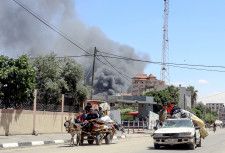 7日、イスラエル軍による空爆で煙が上がる中、パレスチナ自治区ガザの最南部ラファから避難する人々（ゲッティ＝共同）