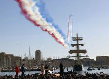 フランス南部マルセイユの旧港に到着した聖火をのせた帆船。その上空を空軍機がカラースモークで彩った＝8日（共同）