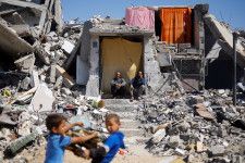 イスラエルの攻撃で破壊された自宅に座る人たち＝14日、パレスチナ自治区ガザ南部ハンユニス（ロイター＝共同）