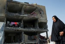 イスラエル軍の攻撃で破壊された家の前を歩くパレスチナ人の女性＝22日、ガザ南部ラファ（ロイター＝共同）