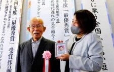 表彰式後、妻千恵子さんの遺影を持つ孫に付き添われ、受賞作に込めた思いを語る長倉幸夫さん（左）＝２日午後、宮崎市民プラザ