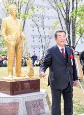 金色に輝くほぼ等身大の銅像とともに、笑顔を見せる加山さん＝11日、市役所前広場